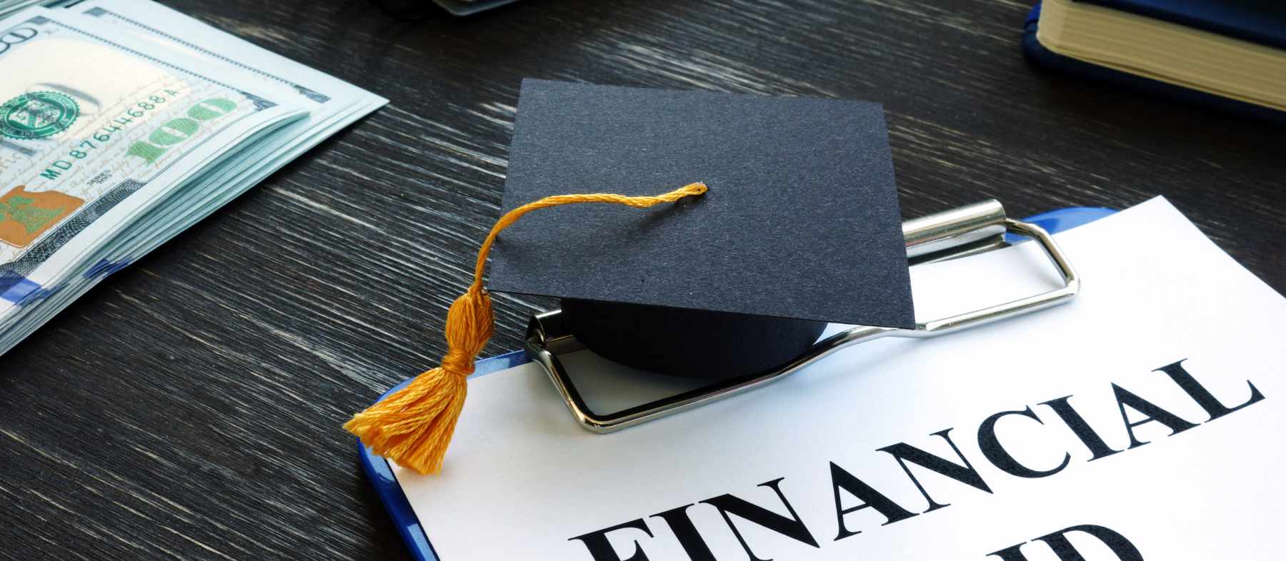 A small graduation cap sits on top a desk with a financial aid application