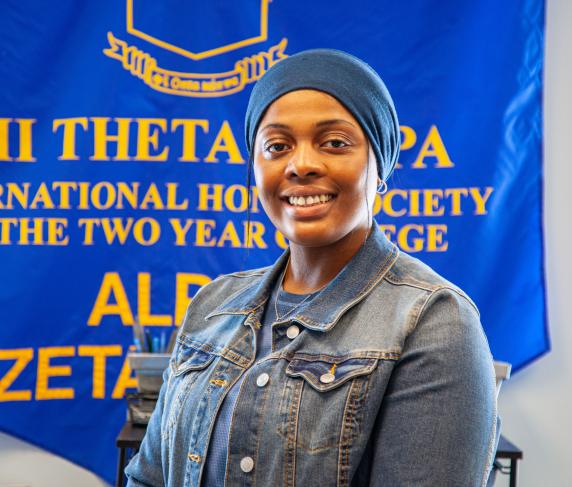 A female PTK student smiles while standing in front of a large blue PTK banner