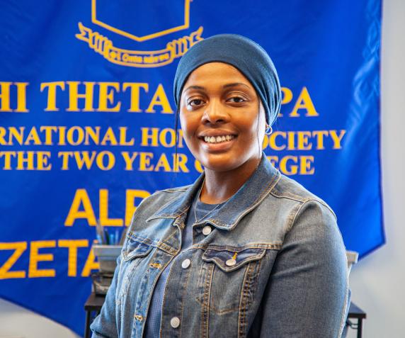 A female PTK student smiles while standing in front of a large blue PTK banner