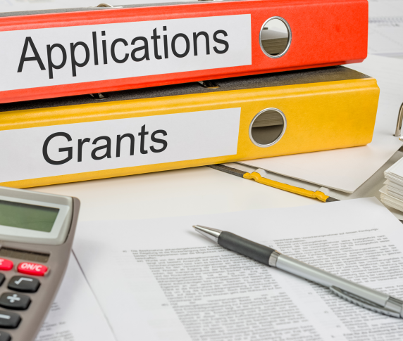 Two binders on a desk with the words ‘applications’ and ‘grants’ on them 