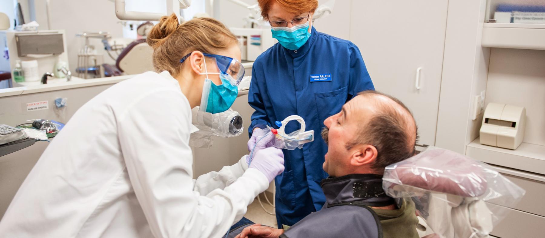 A student and instructor attend to a patient in the dental lab