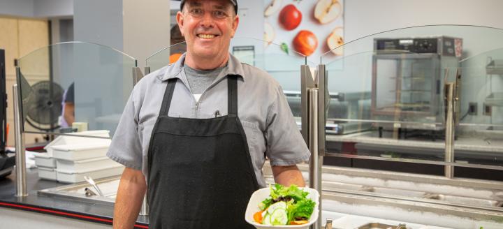 A man working a cafeteria holds a salad in hand