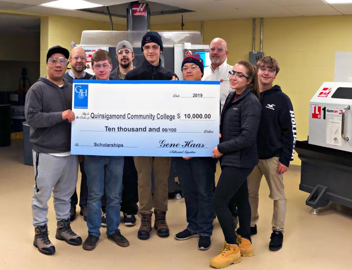 Manufacturing students and professors hold up a giant check in the advanced manufacturing lab