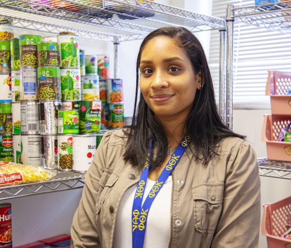 A woman stands next to shelves in the food pantry