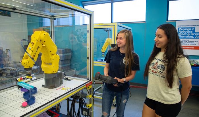 QCC graduate Anna Israelian (left) shows Jessica Calle how to use a FANUC robot.