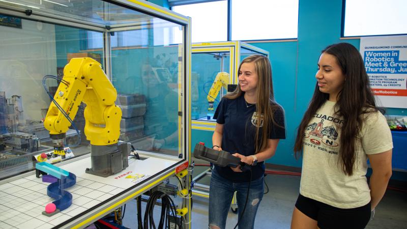 QCC graduate Anna Israelian (left) shows Jessica Calle how to use a FANUC robot.
