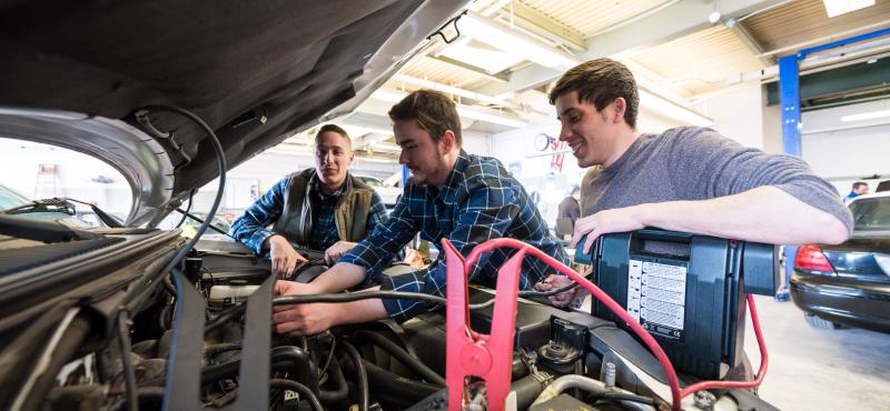 A professor oversees as two students work on a vehicle