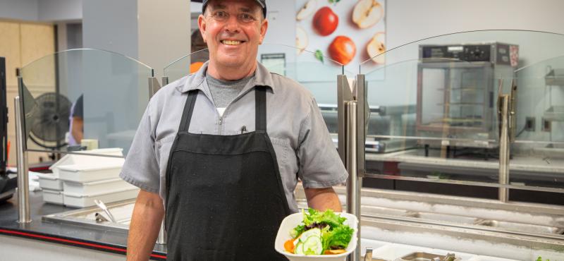 A man working a cafeteria holds a salad in hand